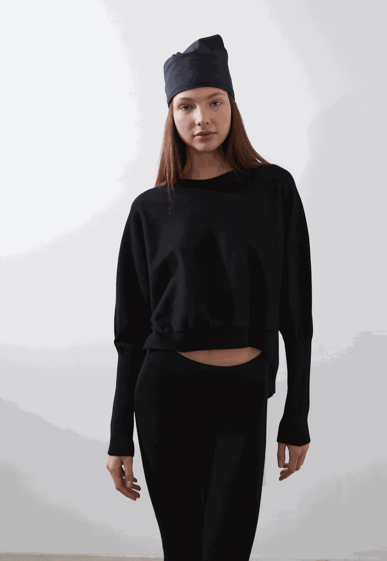 ARMERS Pullover in black with drop sleeves and high-low bodice, modeled by woman in black leggings.