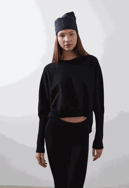 ARMERS Pullover in black with drop sleeves and high-low bodice, modeled by woman in black leggings.