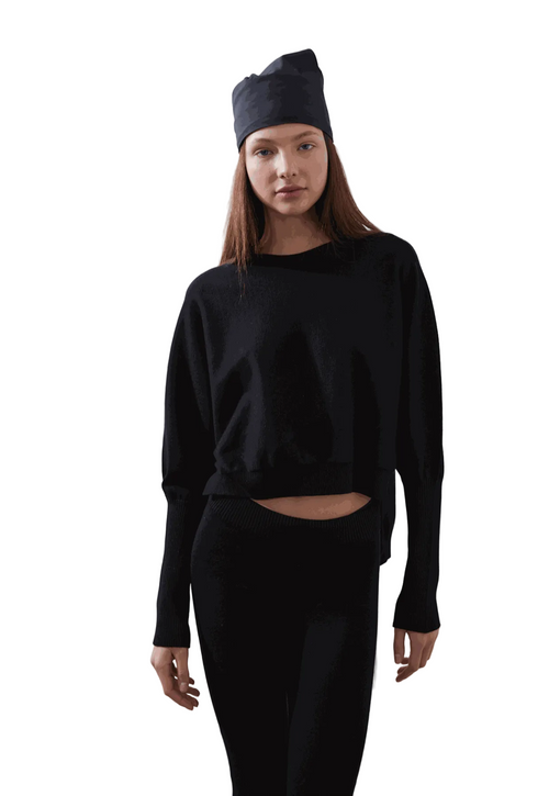 ARMERS Pullover in black with drop sleeves and high-low bodice, modeled by woman in black leggings.